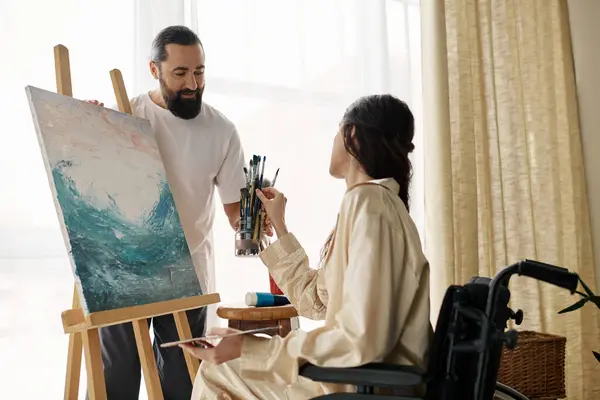 Loving cheerful couple of bearded man and disabled woman painting on easel together at home — Stock Photo