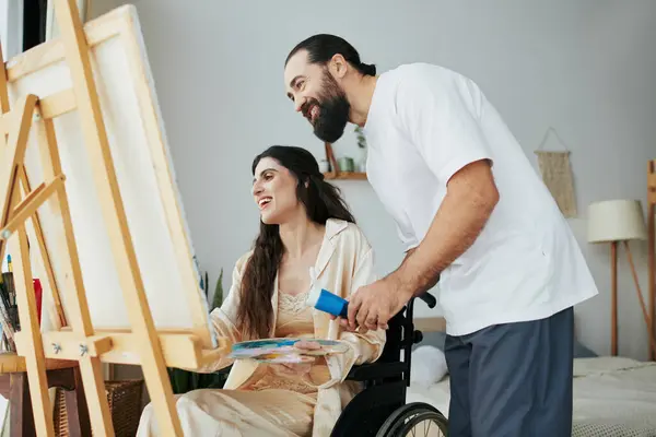 Loving jolly husband helping his inclusive good looking wife to paint on easel while at home — Stock Photo