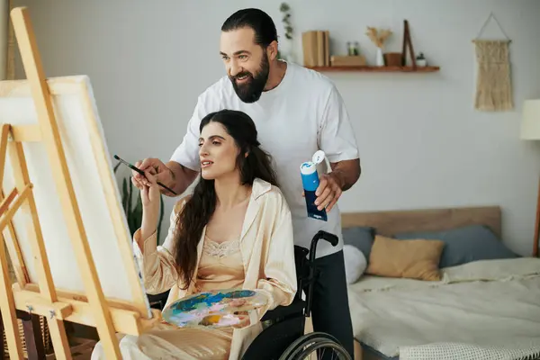 Caring jolly husband helping his inclusive good looking wife to paint on easel while at home — Stock Photo