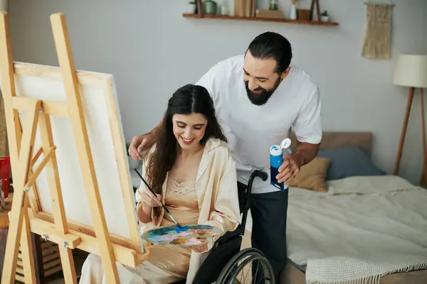 Premurosa coppia allegra di uomo barbuto e disabili pittura donna sul cavalletto insieme a casa — Foto stock