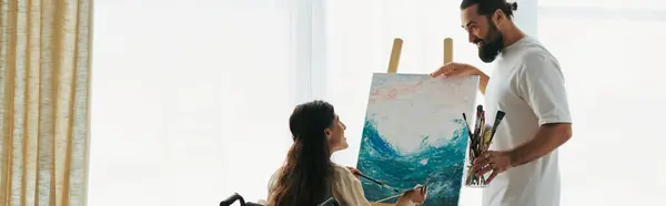 Joyous husband helping his inclusive beautiful wife on wheelchair to paint on easel, banner — Stock Photo