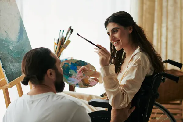 Caring jolly husband helping his inclusive good looking wife to paint on easel while at home — Stock Photo