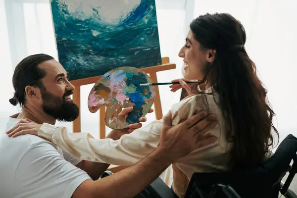 Appealing woman with mobility disability painting on easel next to her cheerful bearded husband — Stock Photo