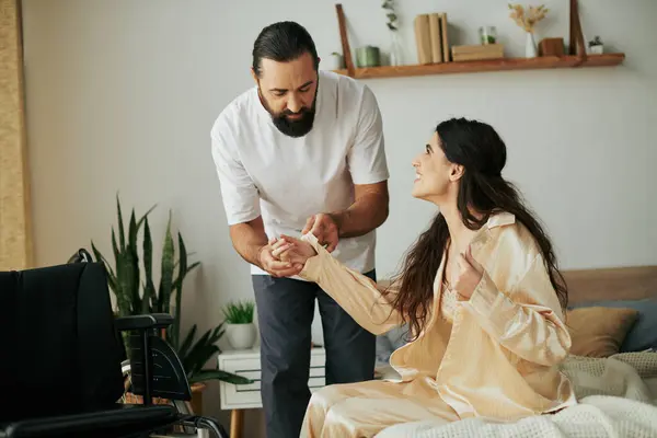 Cheerful loving man in homewear helping his disabled wife to change into pajama in bedroom at home — Stock Photo