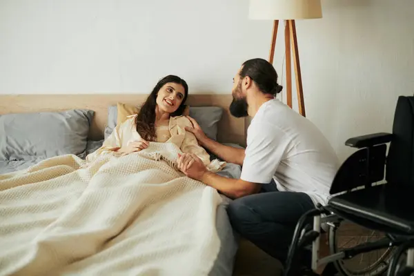 Bella donna gioiosa con disabilità motoria sdraiata a letto accanto al suo marito barbuto amorevole — Foto stock