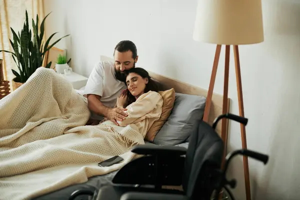 Atractiva mujer alegre con discapacidad de movilidad tumbada en la cama junto a su marido barbudo amoroso - foto de stock