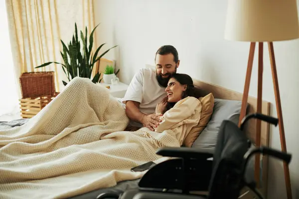 Attraente donna gioiosa con disabilità motoria sdraiata a letto accanto al marito amorevole barbuto — Foto stock