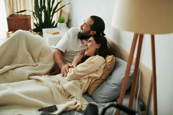 Atractiva mujer alegre con discapacidad de movilidad tumbada en la cama junto a su marido barbudo amoroso - foto de stock