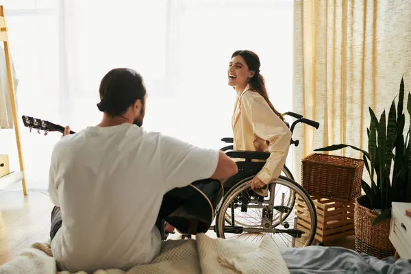 Gioiosa donna con disabilità in sedia a rotelle guardando il marito barbuto suonare la chitarra per lei — Foto stock