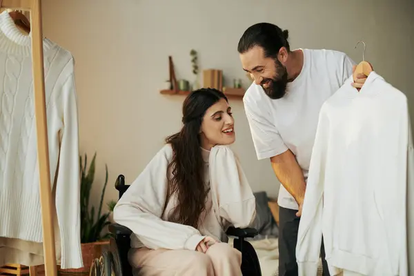 Bearded caring man helping his inclusive wife on wheelchair to get dressed while in bedroom — Stock Photo