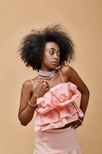 Мрійлива афроамериканська дівчина 20-х років позує в персиковому рюші зверху і пастельній спідниці на бежевому тлі — стокове фото