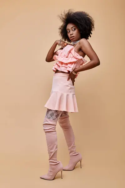Young african american model posing in peach ruffle top and over-knee boots on beige backdrop — Stock Photo