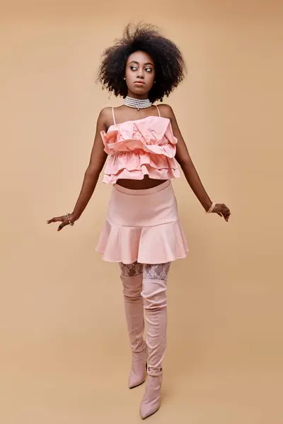 Attractive young african american model posing in peach ruffle top and over-knee boots on beige — Stock Photo