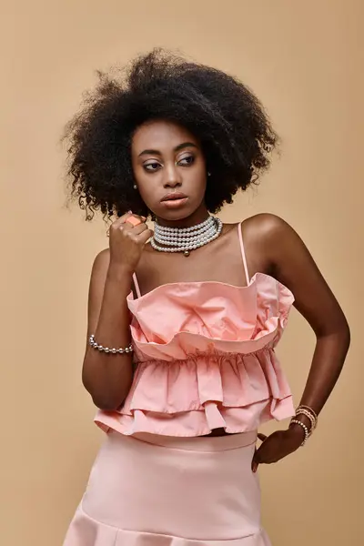 Pretty dark skinned model with curly hair posing in pastel peach ruffled top on beige background — Stock Photo