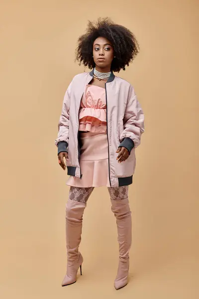 African american girl in 20s, posing in peach outfit with jacket and over-knee boots on beige, style — Stock Photo
