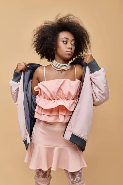 African american girl in 20s, posing in peach outfit with jacket on beige background, color of year — Stock Photo