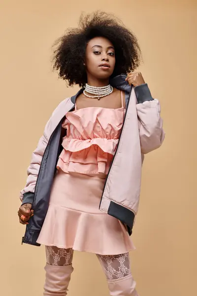 Mujer afroamericana en los años 20, posando en traje de pastel con chaqueta sobre fondo beige, pelusa de melocotón - foto de stock