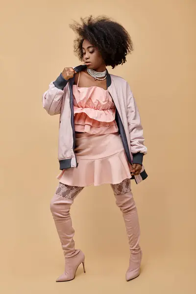 Афроамериканська дівчина в 20-х, позує в персиковому вбранні з піджаком і надлишковими черевиками на бежевому, 2024 — стокове фото