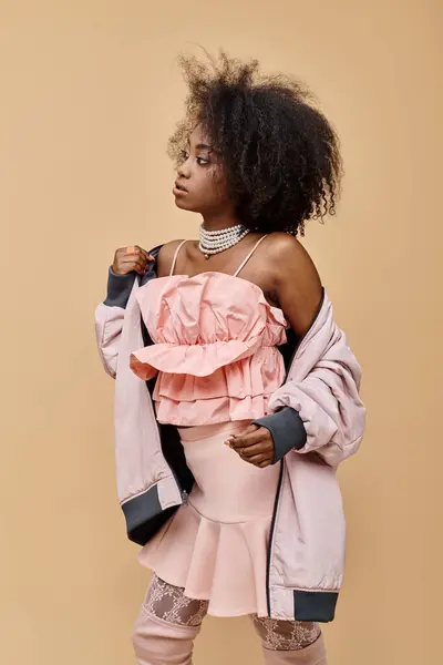 Афро-американська молода жінка позує в пастельному вбранні з курткою на бежевому фоні, персиковий фузі — стокове фото