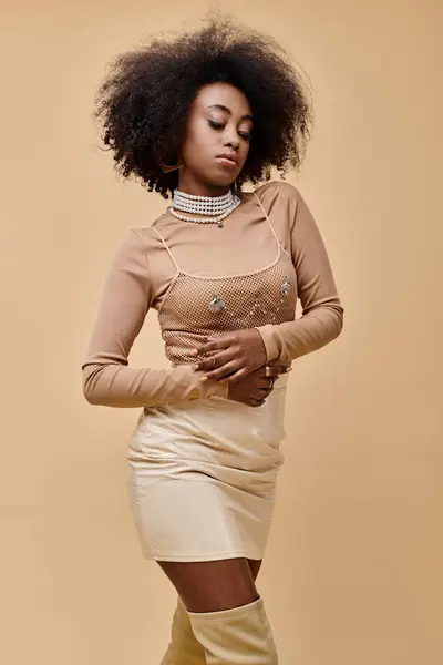 Young african american woman with curly hair posing in stylish pastel outfit on a beige backdrop — Stock Photo