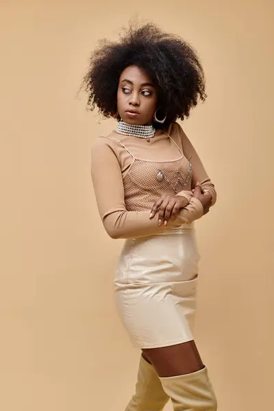 Joven mujer afroamericana con el pelo rizado posando en traje de melocotón pastel sobre fondo beige - foto de stock
