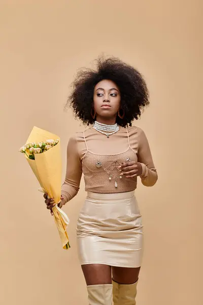 Young african american model posing in pastel peach outfit and holding bouquet on beige backdrop — Stock Photo