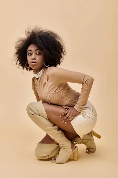 Modèle afro-américain bouclé dans une tenue élégante de couleur pastel et des bottes haut de cuisse assis sur beige — Photo de stock