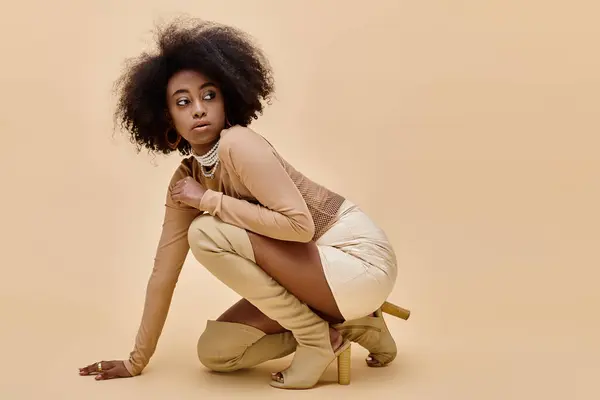 Молода афроамериканська модель в стильному пастельному вбранні і черевиках на стегнах позує на бежевому — стокове фото