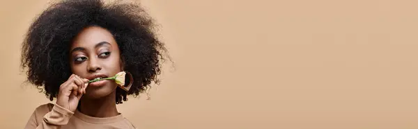 Encaracolado afro-americano mulher com pequena rosa nos dentes em fundo bege, pêssego fuzz banner — Fotografia de Stock