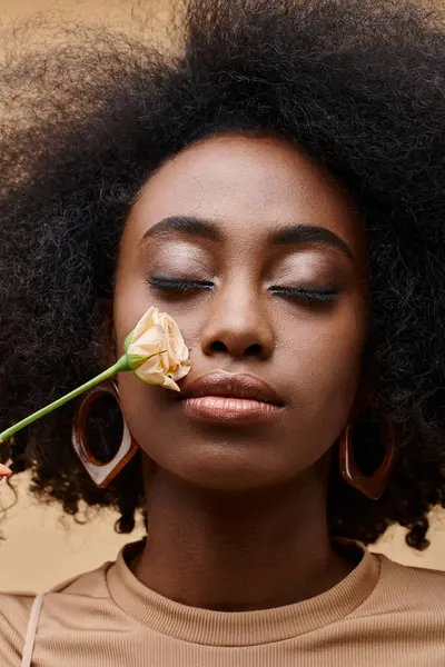 Sensual and curly african american girl in 20s holding small rose near her cheek, peach fuzz — Stock Photo