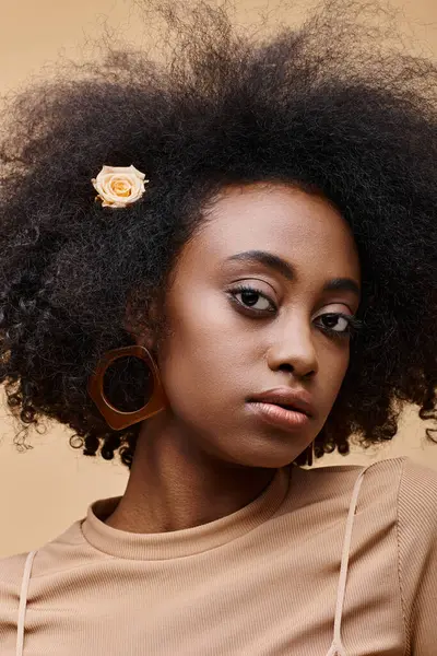 Sensual young african american girl with small rose in curly hair on beige background, peach fuzz — Stock Photo