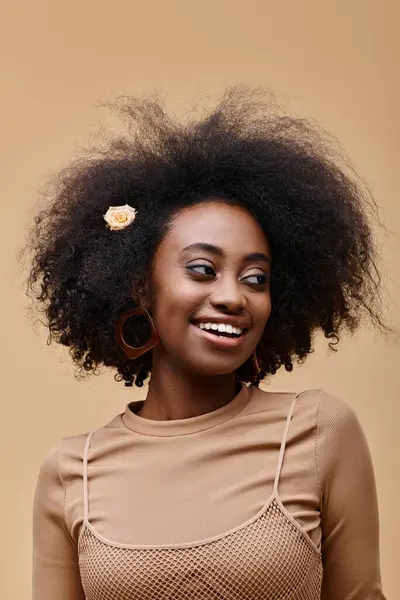 Smiling young african american girl with small rose in curly hair on beige background, peach fuzz — Stock Photo