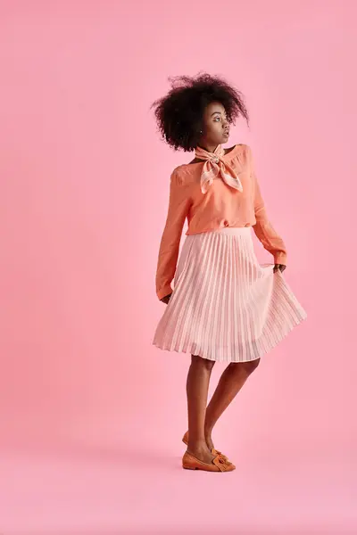 Young african american woman in peach blouse and midi skirt strikes a pose on pastel pink background — Stock Photo