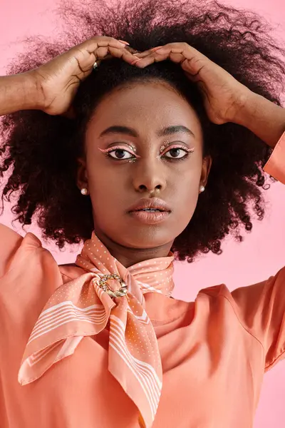 Portrait of african american woman in peach blouse and neck scarf adjusting hair on pink backdrop — Stock Photo