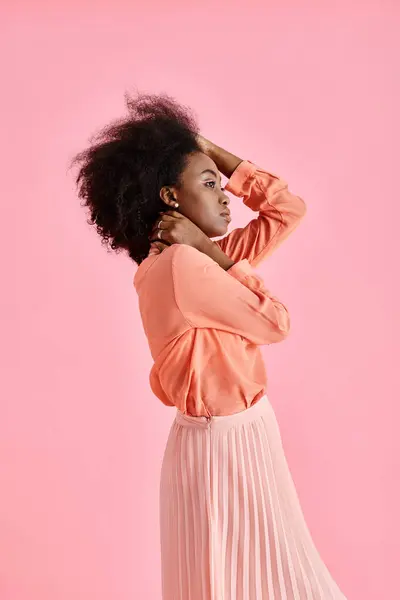 Side view, african american woman in peach blouse, midi skirt and neck scarf posing on pink backdrop — Stock Photo