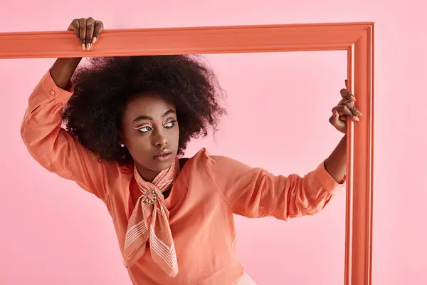 Young african american woman in peach fuzz blouse and neck scarf posing in frame on pink backdrop — Stock Photo