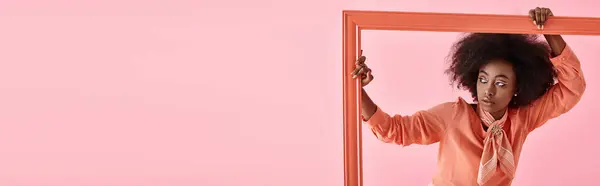 Банер, афроамериканська жінка в персиковій блузці та шарфі шиї позує в рамці на рожевому тлі — стокове фото