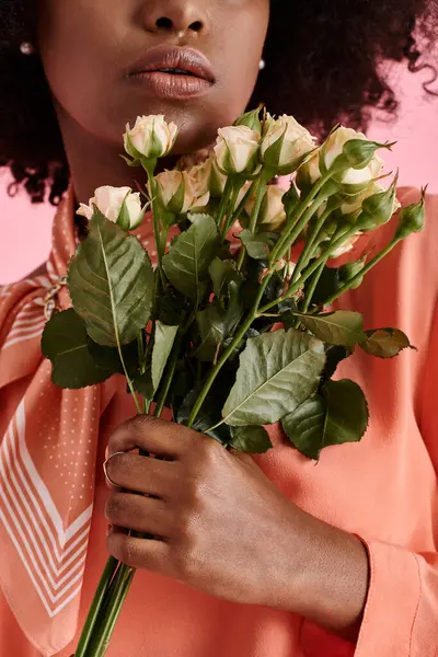 Vista recortada de chica afroamericana en blusa de pelusa de melocotón sosteniendo flores sobre fondo rosa - foto de stock