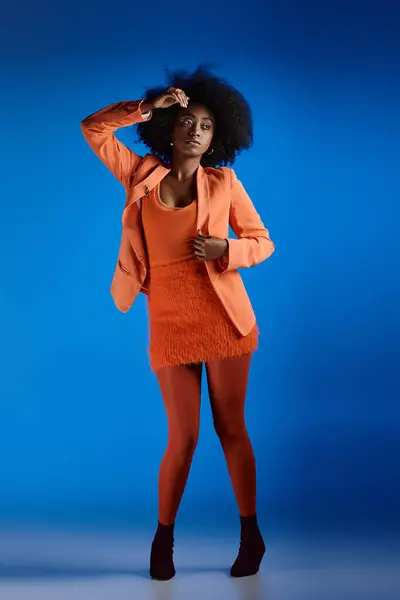 Довольно африканская американская модель в текстурированном платье и блейзере позируя на высоких каблуках, яркий синий фон — стоковое фото