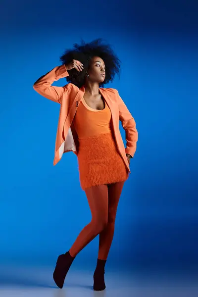 Encaracolado jovem modelo afro-americano em vestido texturizado e blazer posando com a mão no quadril no azul — Fotografia de Stock