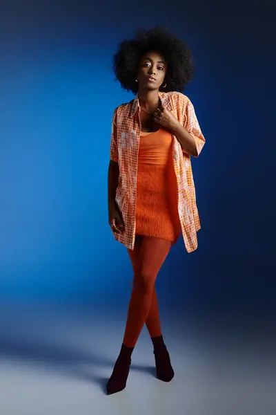 Elegante look de mujer afroamericana bonita en camisa estampada y vestido naranja sobre fondo azul - foto de stock