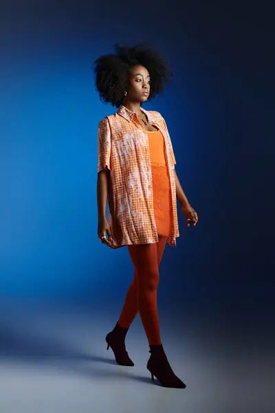 Elegante look de chica afroamericana bonita en camisa estampada y vestido naranja sobre fondo azul - foto de stock