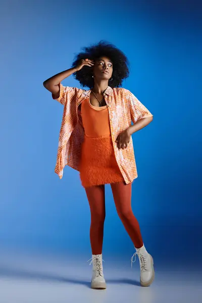 Modèle afro-américain à la mode en chemise à motifs et robe texturée posant sur fond bleu — Photo de stock