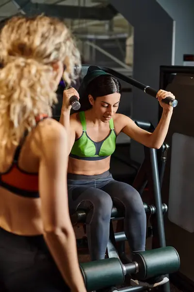 Sportliche Trainerin berät ihren blonden, gut gelaunten Kunden im Fitnessstudio in der Nähe der Schulterpresse — Stockfoto