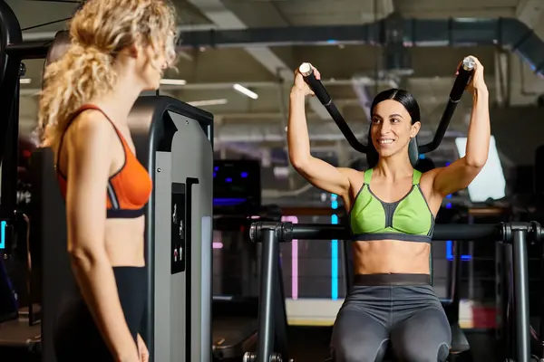 Entrenador femenino deportivo consultando a su cliente alegre rubia en el gimnasio cerca de la máquina de prensa de hombro - foto de stock