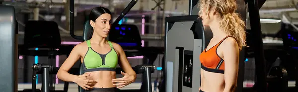 Energetic female coach consulting her joyous client in gym near shoulder press machine, banner — Stock Photo