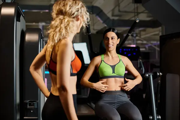 Sportliche brünette weibliche Trainerin berät ihren blonden freudigen Kunden im Fitnessstudio in der Nähe der Schulterpresse — Stockfoto
