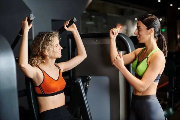 Entraîneur féminin forte consultation de son client joyeux attrayant dans la salle de gym près de la presse épaule machine — Photo de stock