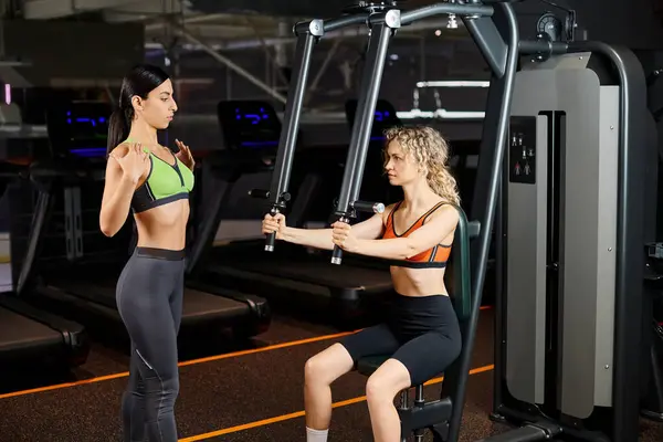 Attractive female coach explaining to her appealing jolly client how to use chest press machine — Stock Photo