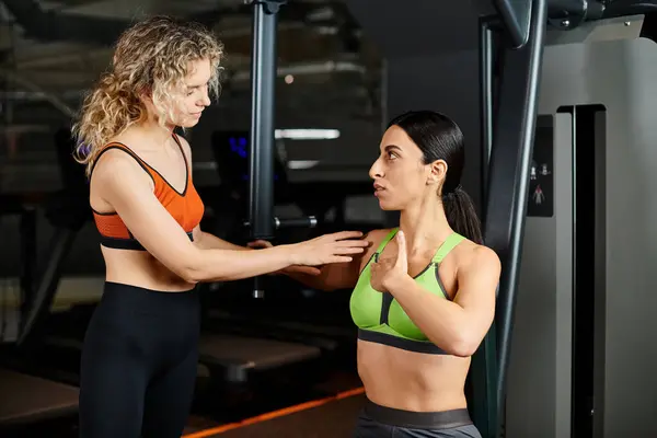 Positive weibliche Trainerin erklärt ihrer ansprechenden, lustigen Klientin, wie man Brustpresse bedient — Stockfoto